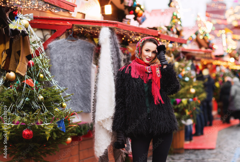 Outdoors lifestyle fashion portrait of stunning blonde young woman. Smiling, walking on the christmas market. Going shopping. Trendsetter. Wearing stylish black fur coat and scarf. Festive mood