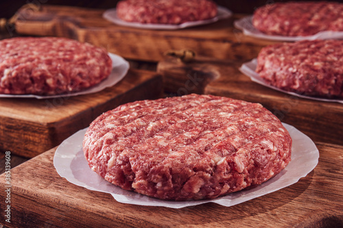 Raw hamburgers on cutting board with wood pile background - Close-up