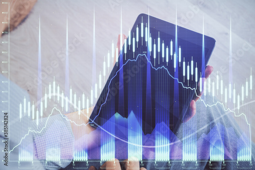 Double exposure of man's hands holding and using a digital device and forex graph drawing. Financial market concept. © peshkova