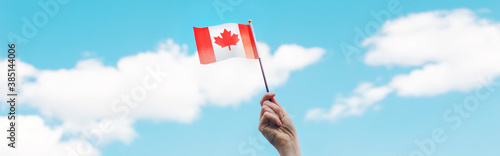 Closeup of woman human hand arm waving Canadian flag against blue sky. Proud citizen man celebrating national Canada Day on 1st of July outdoors. Web banner header. © anoushkatoronto