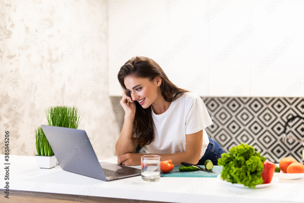 Beautiful young woman cooking with receipt on laptop in the kitchen Beautiful young woman cooking with receipt on laptop in the kitchen