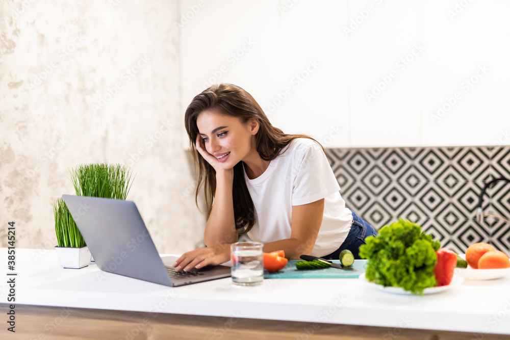 Young Woman enjoying cooking looking for a recipe on the laptop in the kitchen Young Woman enjoying cooking looking for a recipe on the laptop in the kitchen