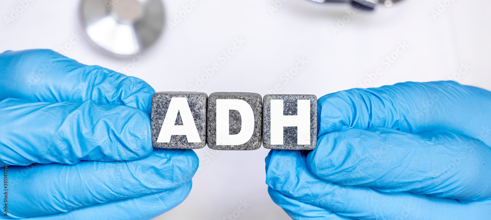 ADH Antidiuretic hormone - word from stone blocks with letters holding by a doctor's hands in medical protective gloves ADH Antidiuretic hormone - word from stone blocks with letters holding by a doctor's hands in medical protective gloves