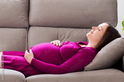 Portrait of a tired pregnant woman sleeping on a couch in the living room at home
