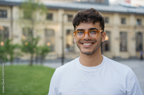 Authentic portrait of young successful Indian man wearing stylish eyeglasses, standing on the street. Handsome asian model posing for pictures, looking at camera, smiling