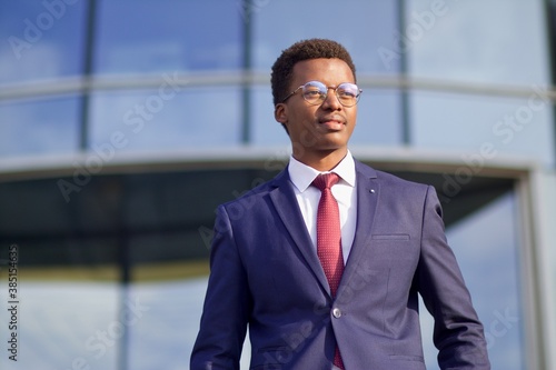 Portrait of young successful confident businessman in formal suit, tie and glasses outdoors business building. Black African Afro American handsome man, office worker