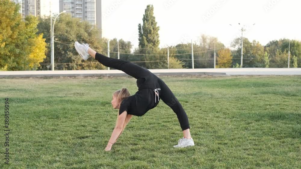Beautiful girl is doing exercises in the fresh air. Against the background of the city. Gymnastics, acrobatics. Training on green grass. Slow motion. Shot in 4k Beautiful girl is doing exercises in the fresh air. Against the background of the city. Gymnastics, acrobatics. Training on green grass. Slow motion. Shot in 4k