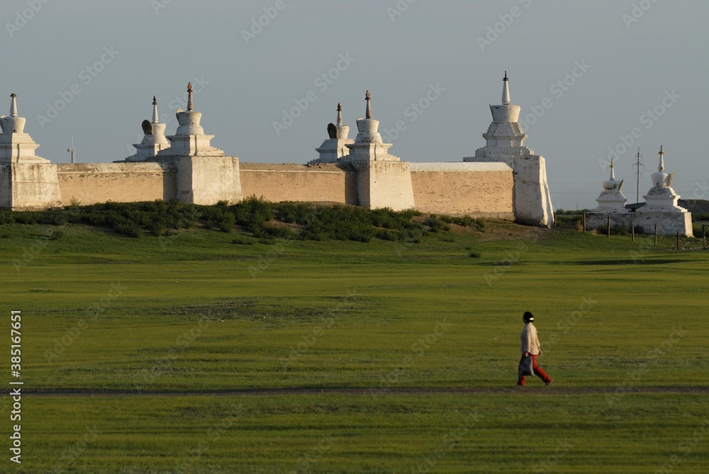Mongolian woman walking in front of the stupa of the outer wall of the ...