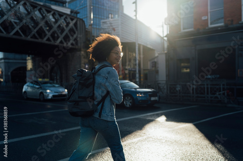 Afro young woman with backpack crossing street in city