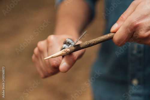 Close-up of mid adult man cutting wood with penknife in forest photo