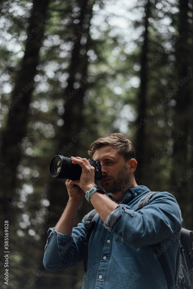 Close-up of male hiker photographing with camera while standing in forest Close-up of male hiker photographing with camera while standing in forest