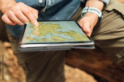 Close-up of man's hands using map over digital tablet in forest photo