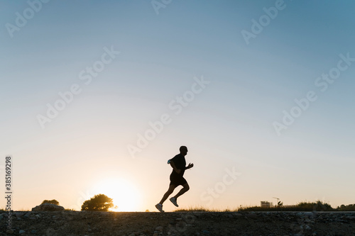 Silhouette of senior athlete jogging against clear sky during sunset photo