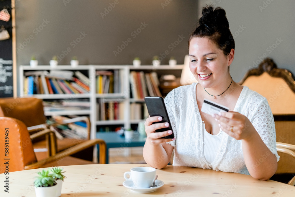 Smiling woman with coffee on table doing online shopping over mobile phone in cafe Smiling woman with coffee on table doing online shopping over mobile phone in cafe