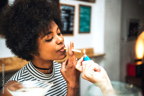 Close-up of man lightning cigarette held by girlfriend in bar