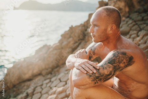 Tattooed nudist sitting on volcanic rocks by the sea photo