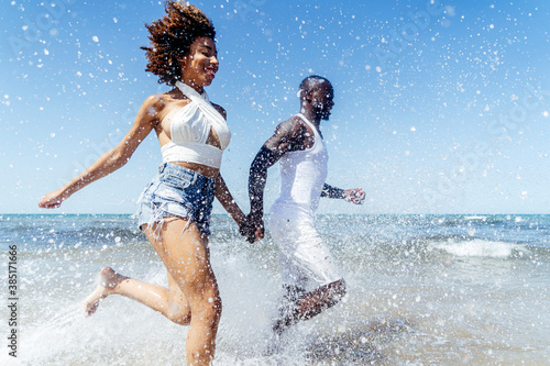 Fotografie Cheerful couple running in sea against clear sky during summer
