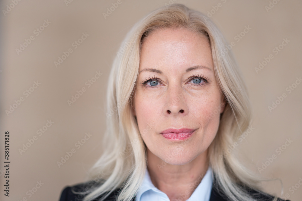 Close-up of confident female entrepreneur with blond hair against wall in office Close-up of confident female entrepreneur with blond hair against wall in office