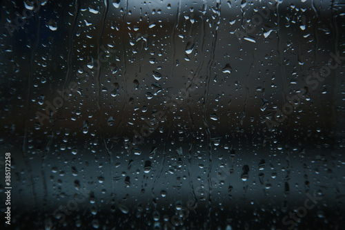 Blurry rain drops on window glasses surface with cloudy background. Dramatic background concept