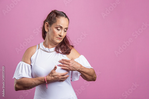 Mujer madura con cáncer de mama en fondo rosado tocando su seno  photo