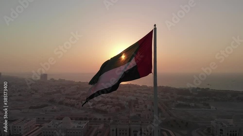 Silhouette, Flag of the United Arab Emirates waving in the wind, Sky and Sun Background, The national symbol of UAE over Sharjah's Flag Island, United Arab Emirates, 4K video photo