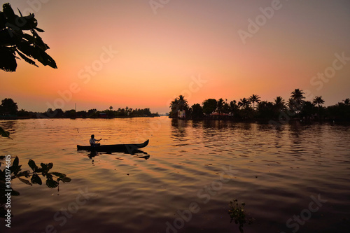 A boat sailing over backwaters in Kerala during sunset.
