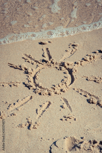 Shape of sun on sand at beach and incoming sea wave. Summer, vacation time and tourism