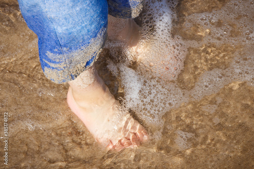 Feet of little boy on sand in sea. Summer time
