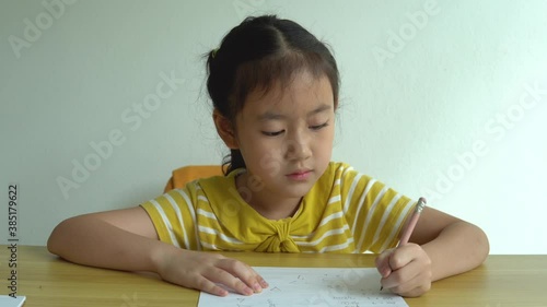 Cute smart primary school child girl learning writing doing math homework sit at home table, adorable pretty little preschool kid studying alone making notes, children elementary education concept