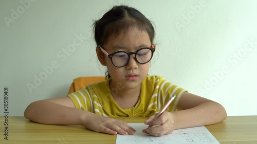 Cute smart primary school child girl learning writing doing math homework sit at home table, adorable pretty little preschool kid studying alone making notes, children elementary education concept