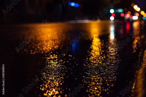 selective focus of night city and car during rain, with unfocused lights. Water on the asphalt and abstract image of side lights in the city