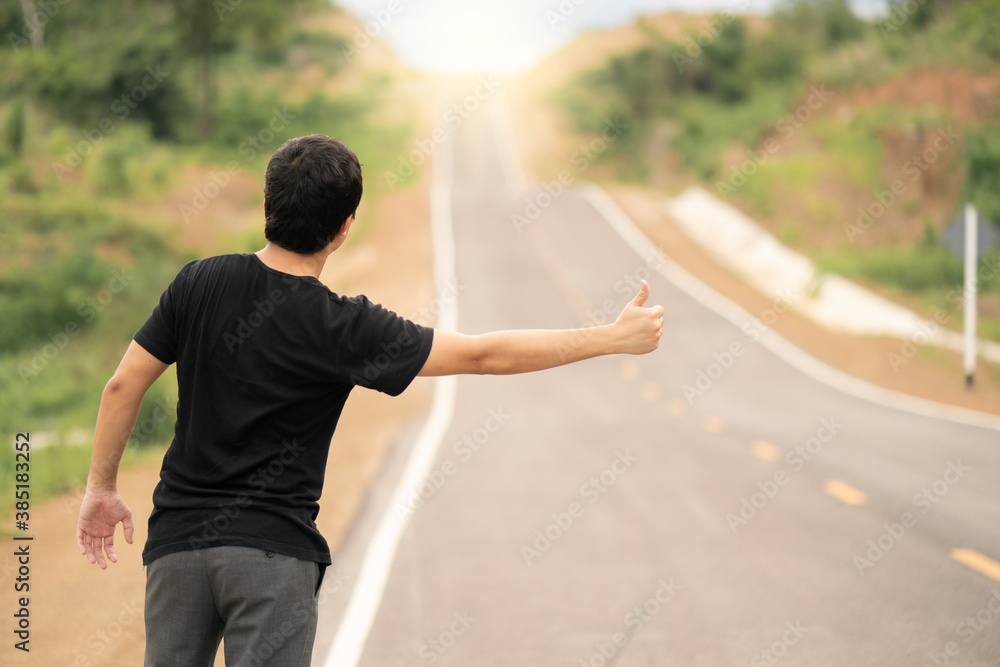 Man hitchhiking on the road, empty rural curve, asphalt road way. Rear view. Man hitchhiking on the road, empty rural curve, asphalt road way. Rear view.