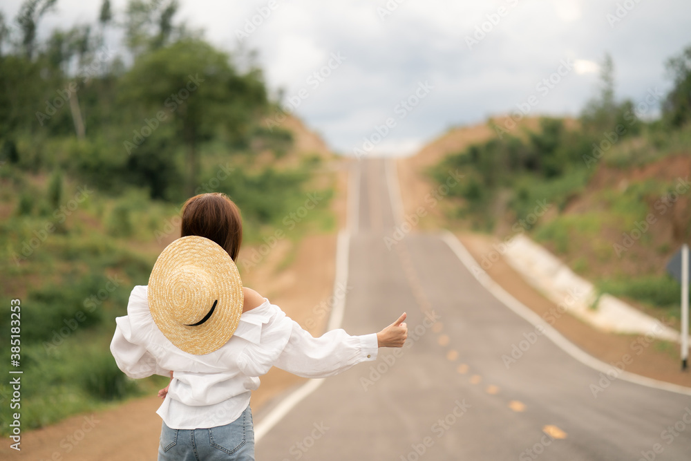 Fototapeta premium Woman hitchhiking on the road, empty rural curve, asphalt road way. Rear view.