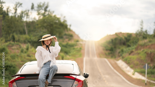 Woman sitting on the car, pose with car in beautiful empty rural curve, asphalt road way.