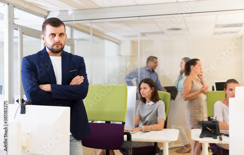 Portrait of confident businessman with arms crossed in busy modern coworking space