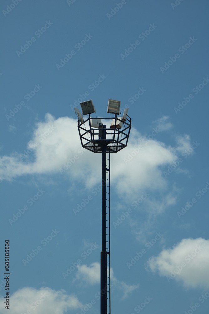 Torre de iluminación en estacionamiento con cielo azul y nubes de fondo. Torre de iluminación en estacionamiento con cielo azul y nubes de fondo.