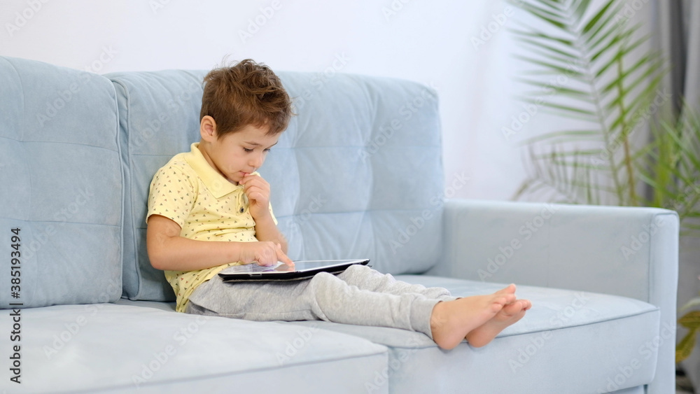boy home sits on the sofa play looks tablet cartoons games movies movie boy home sits on the sofa play looks tablet cartoons games movies movie