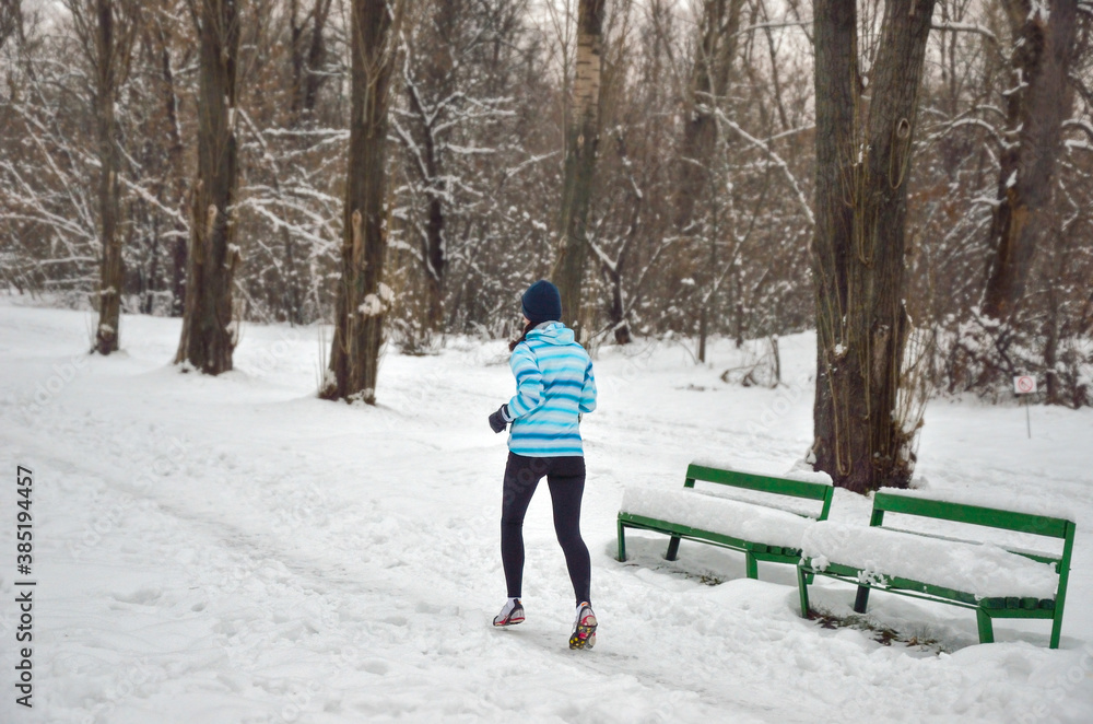 Active happy woman runner jogging outdoors in snowy park in winter, healthy lifestyle, sport and running concept
