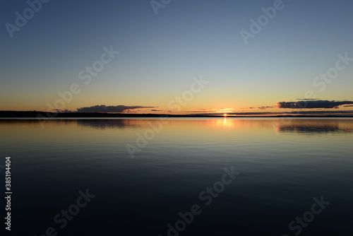 Sunset on the horizon over a calm water surface lake