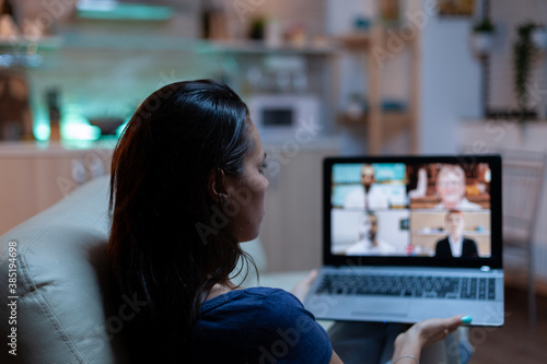 Freelancer having virtual conversation with colleagues on laptop sitting on couch in pijamas. Remote worker discussing during online meeting consulting with team on videocall using internet technology