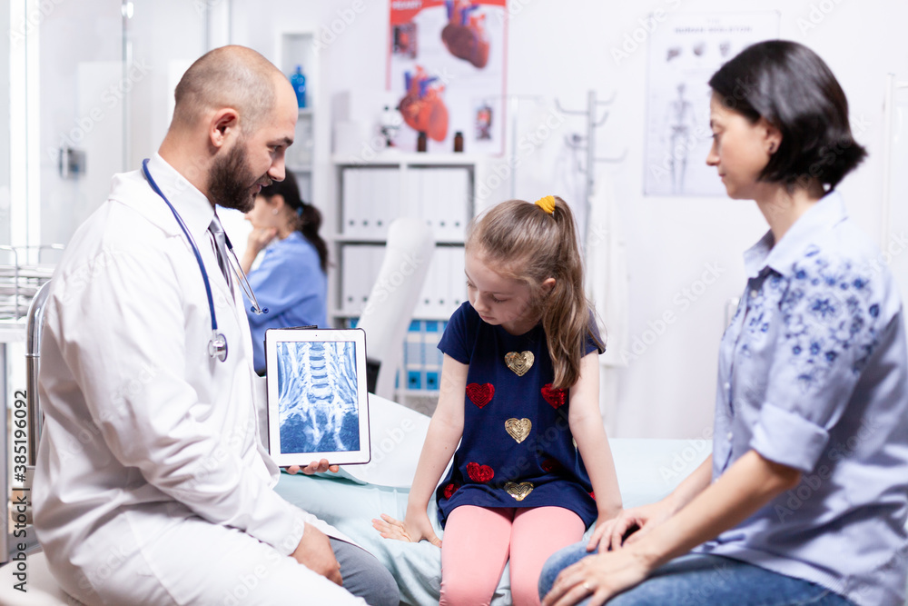 Fototapeta premium Pediatrician explaining radiography for sick child and mother in hospital office. Healthcare physician specialist in medicine providing health care services treatment examination.