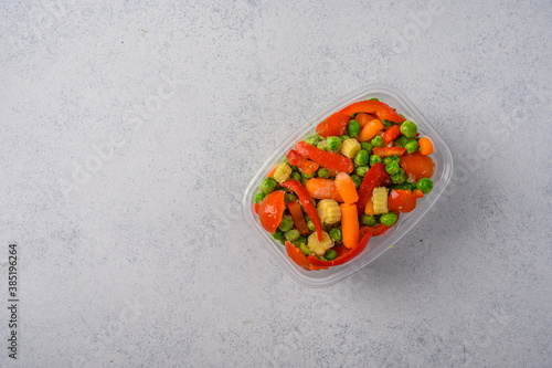 Frozen vegetables corn, red pepper, peas, carrots, tomatoes in plastic tray on an gray background top view, copy space for text