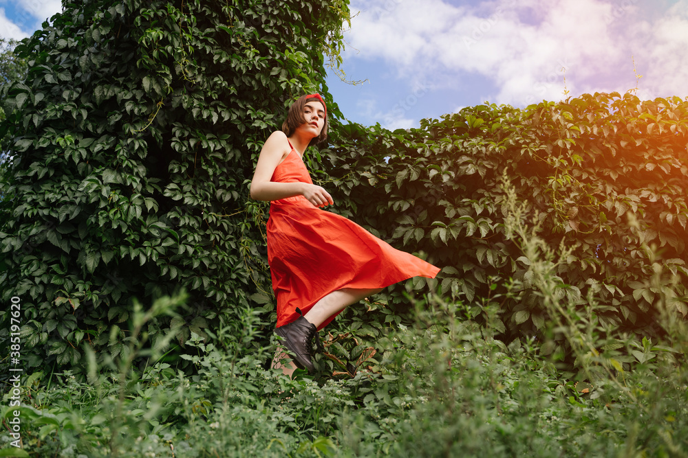 beautiful young rebel brunet girl in red dress in green park bushes walking  in black shoes. Color contrast expressive fashion style move. Conceptual  artistic horizontal composition Stylish brutal teen Stock-foto | Adobe