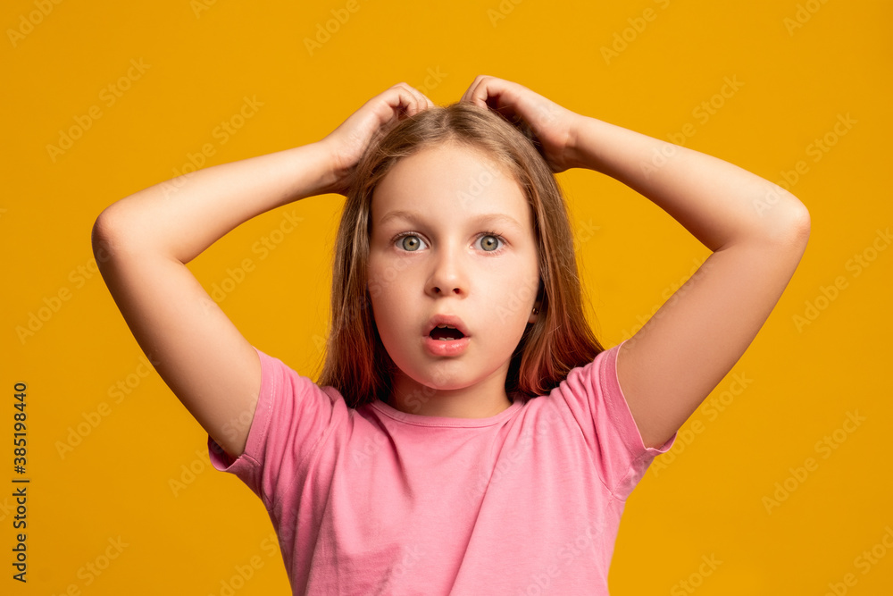 Shocked child. Mistake failure. Hard choice. Tough decision. Portrait of troubled doubtful young girl with hands on head looking at camera with open mouth isolated on orange background. Shocked child. Mistake failure. Hard choice. Tough decision. Portrait of troubled doubtful young girl with hands on head looking at camera with open mouth isolated on orange background.