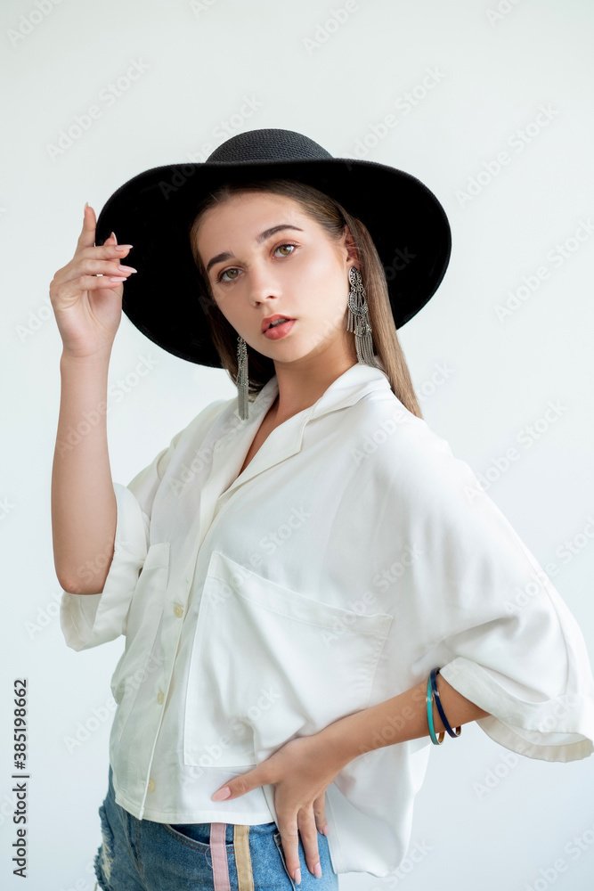 Casual boho style. Trend look. Beautiful woman in straw wide-brimmed black hat vintage earrings white blouse. Looking at camera isolated on neutral. Fashion model. Hipster elegance Casual boho style. Trend look. Beautiful woman in straw wide-brimmed black hat vintage earrings white blouse. Looking at camera isolated on neutral. Fashion model. Hipster elegance