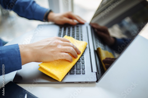 Closeup of the man s hands cleaning laptop s keyboard with a yellow rag and sanitizer to prevent coronavirus spread during global pandemic quarantine. Health care and removing bacteria from gadgets.