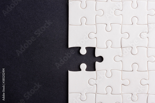 Top view flat lay of paper plain white jigsaw puzzle game texture incomplete or missing piece, studio shot on a black background, quiz calculation concept