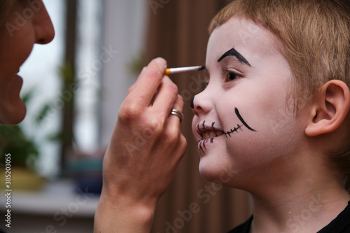 Mother is helping caucasuan son with Halloween makeup indoor photo