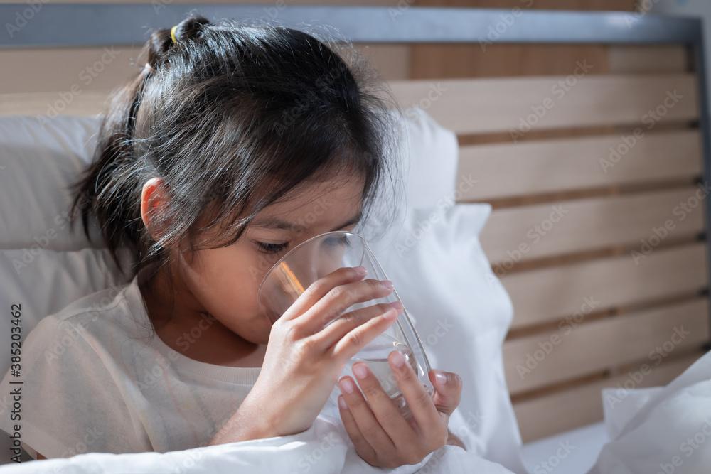 Sick asian child girl is drinking water from a glass after eat medicine in bedroom. Sick child and health care concept. Sick asian child girl is drinking water from a glass after eat medicine in bedroom. Sick child and health care concept.