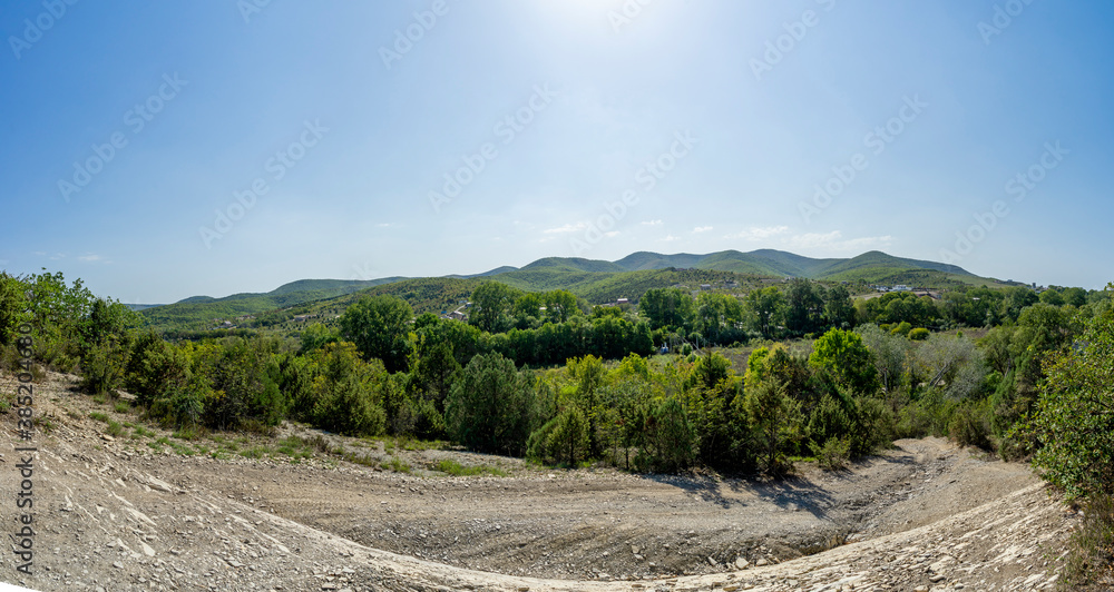Panorama with a view of a dirt road and mountains in the background on a Sunny warm day.